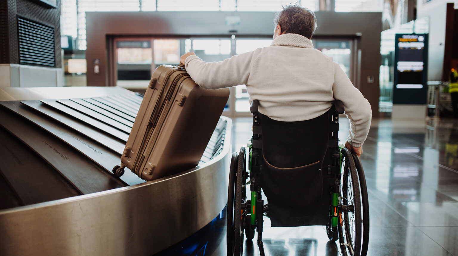 Rear view of a man on wheelchair at airport with his luggage.