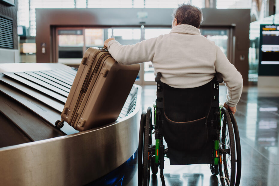 Rear view of a man on wheelchair at airport with his luggage.